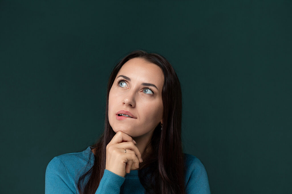 a woman in a blue shirt contemplating with her hand on her chin.